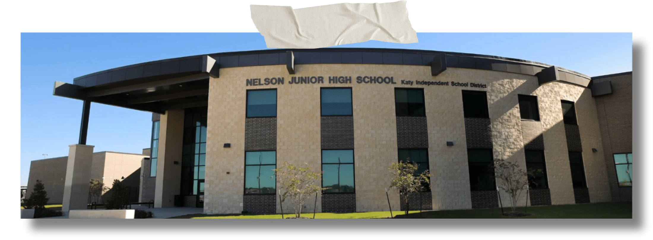 A photo of the curved, modern facade of Nelson Junior High School, a two-story stone and brick building, set against a bright blue sky.